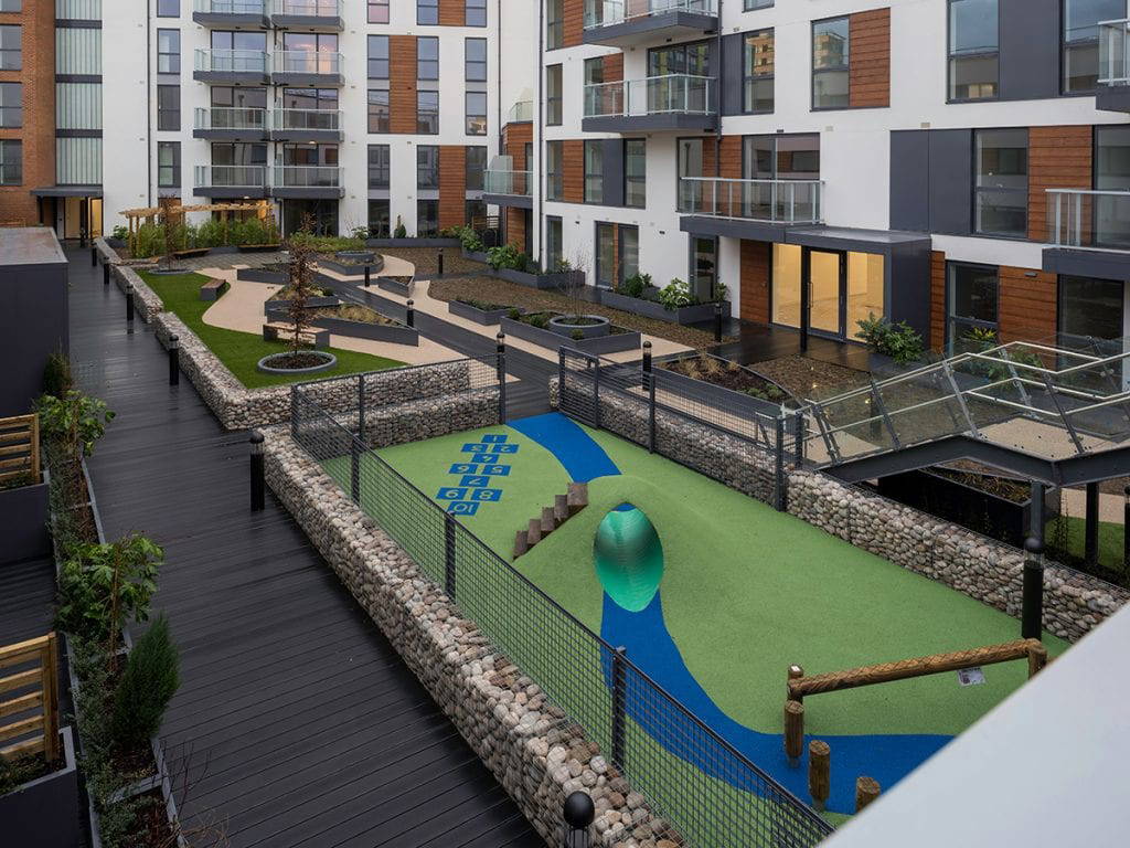 Roof garden play area surrounded by gabion wall and weldmesh fencing and raised planting beds and mounded artificial turf