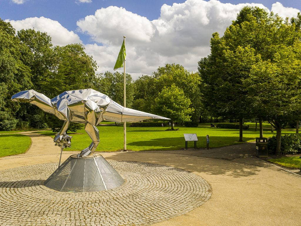 stainless steel dinosaur sculpture in close park within granite sett circle
