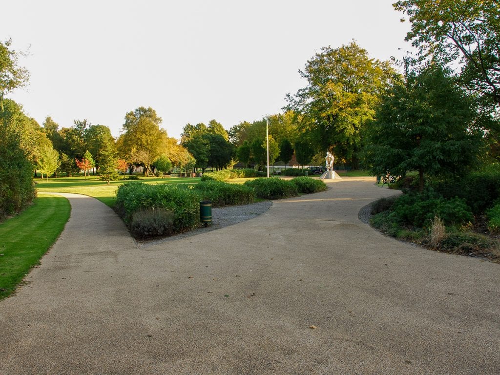 Designed by Nick Atherton , view of Close Park pedestrian entrance with resin bonded gravel, stainless steel dinosaur and arboretum.