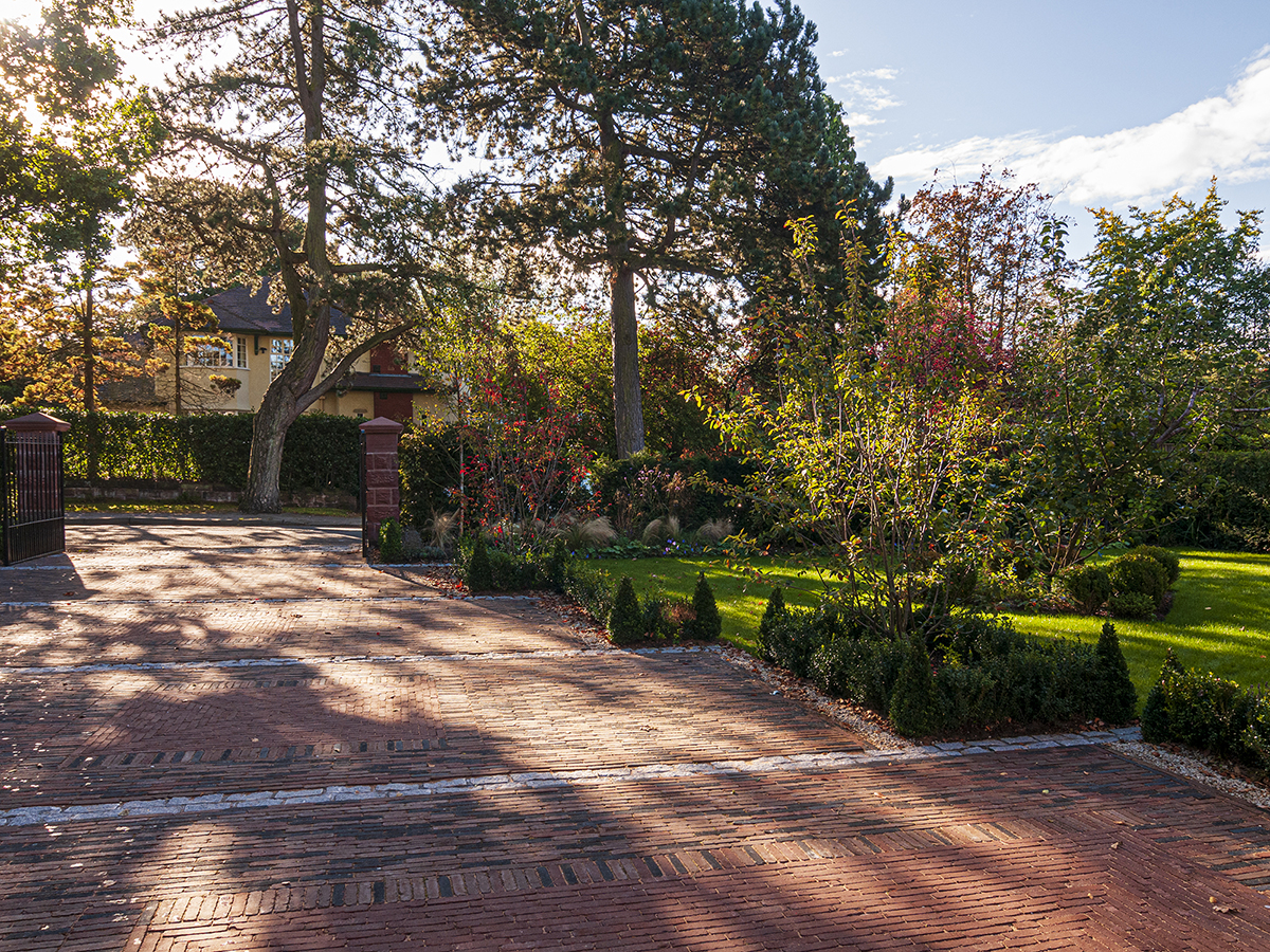 driveway with Belgian pavers and gate pillars box hedge and topiary and large pine trees