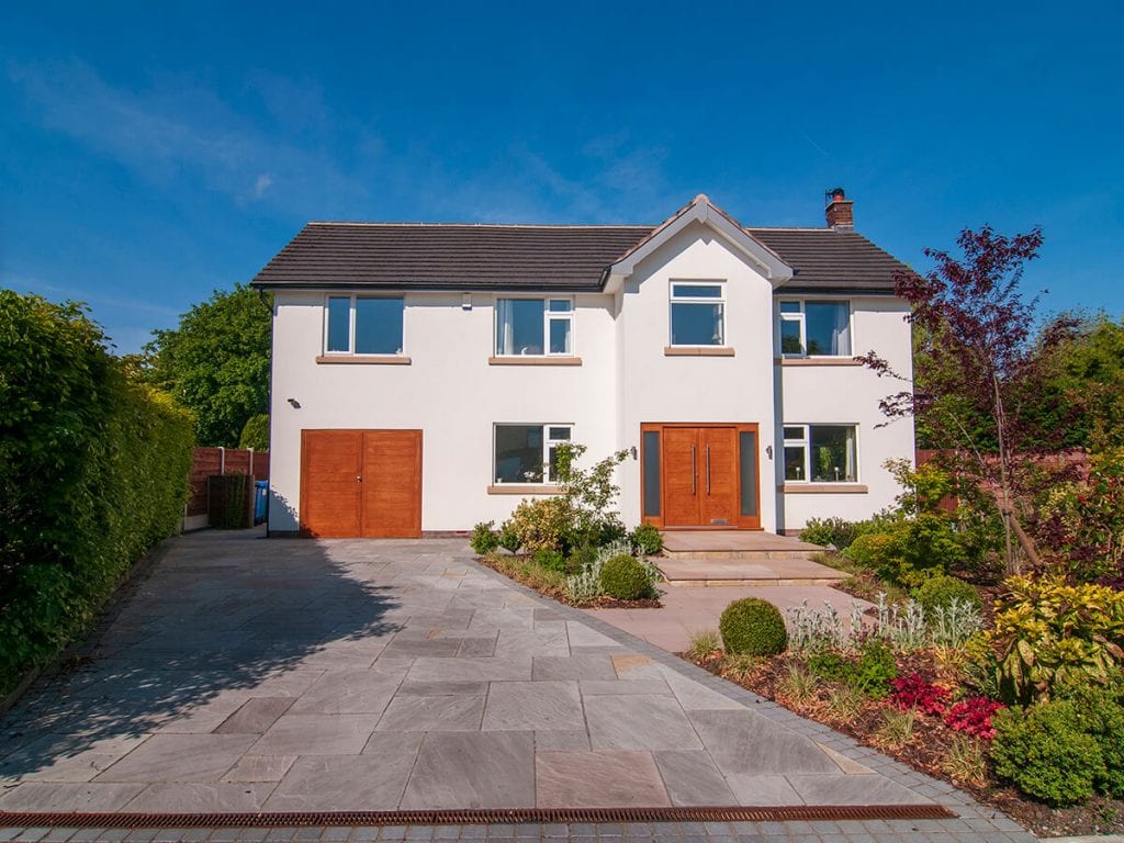 Private residence, Bramhall. A modern detached house with white render. View of front of house with new accoya garage and front doors, new driveway with riven sandstone paving, and front steps with surrounding planting.