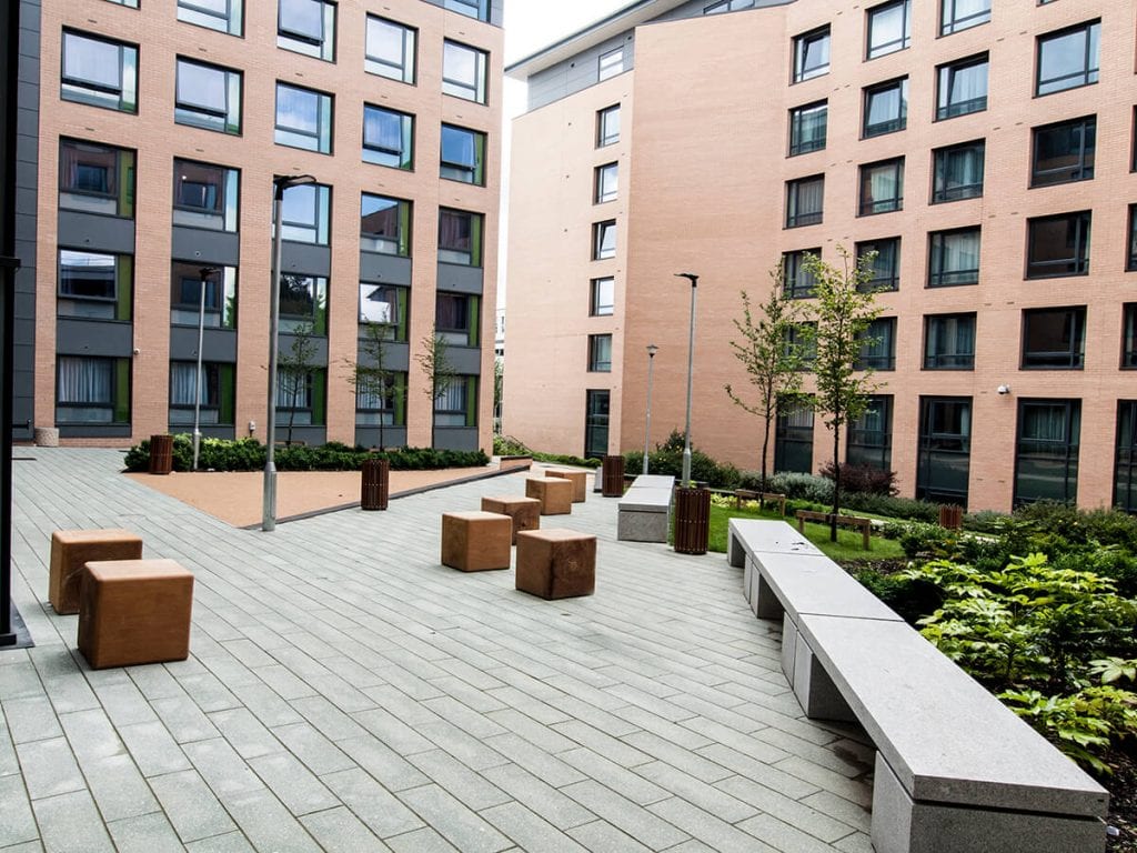 Natural Dimensions designed View of Fountains Court Leeds Trinity University with linear granite bench, individual timber bale seats, plank paving carpinus betulus trees, fatsia and buff resin bound gravel on ramp