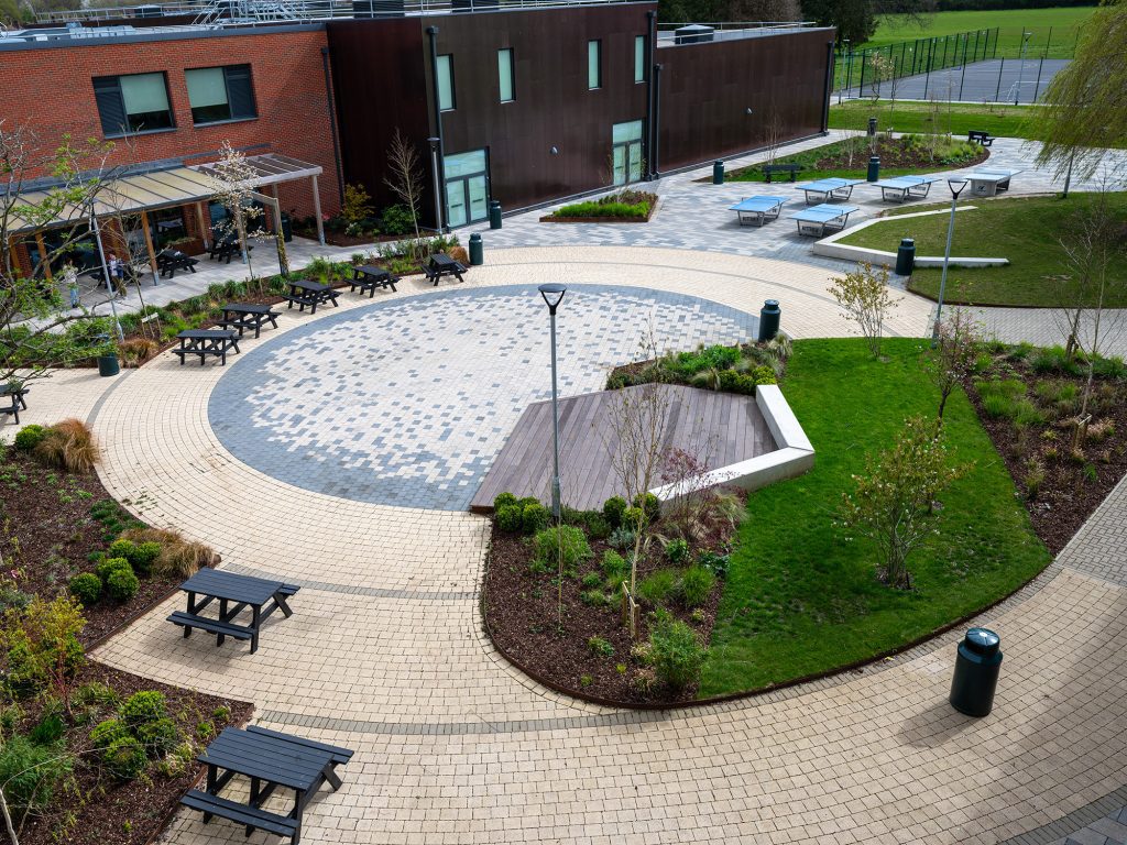 View of biophilic courtyard design with  seat walls, stage, curved paving and table tennis tables 