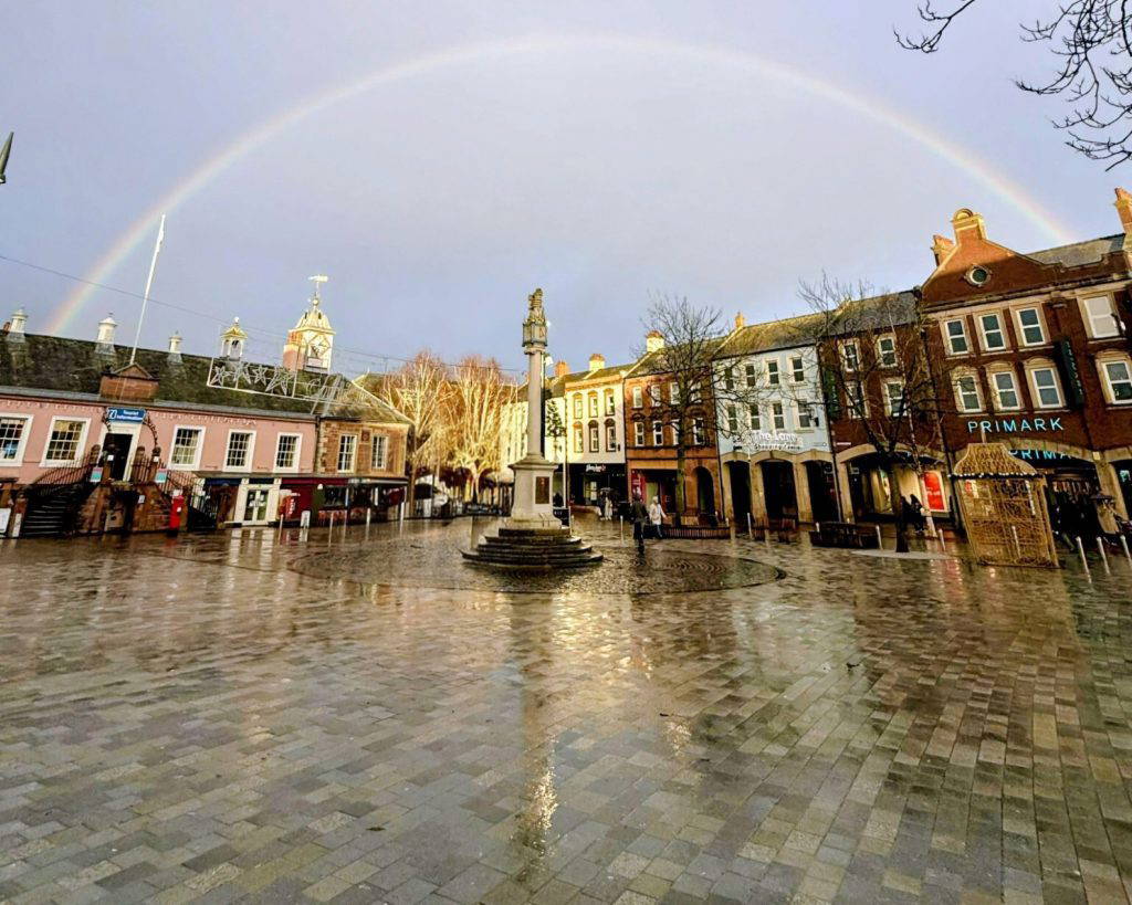 carlisle market cross surrounded by mix of glowing setts underneath rainbow