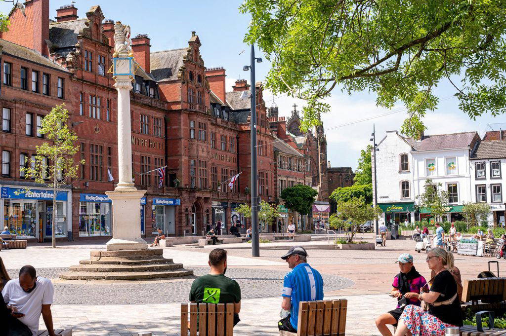 people sitting in Carlisle Market Square in different directions with view of Market Cross